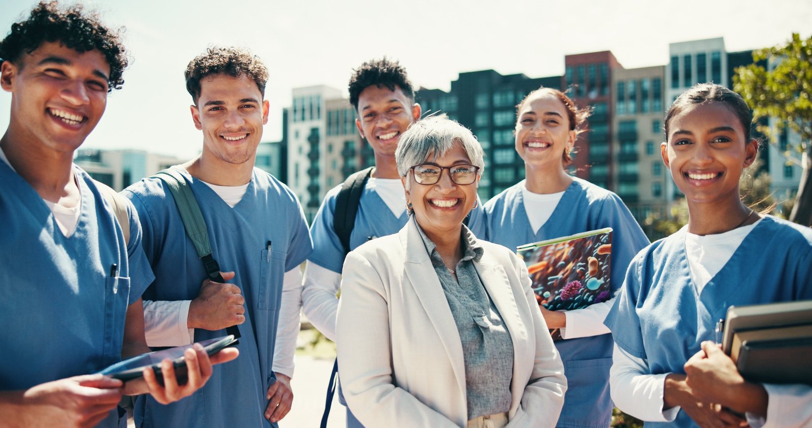 Nurses in scrubs smiling together outdoors with an educator
